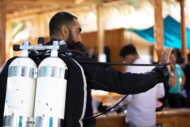 A diver carrying a twinset and cylinders while preparing equipment before a dive