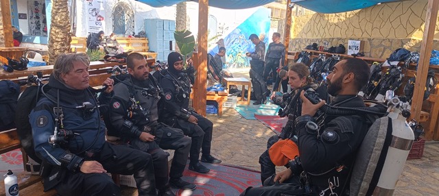 A group of divers in drysuits sitting together before entering the water