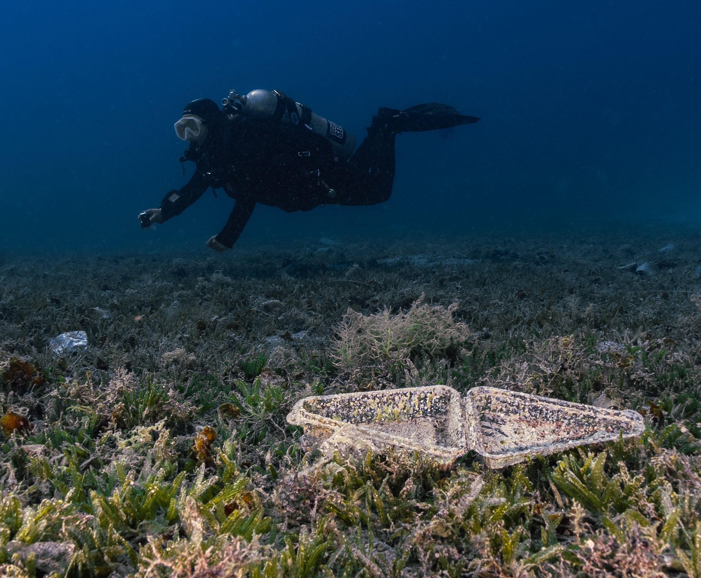 A plastic bag half-buried in the sand on the seabed, tangled with fishing line