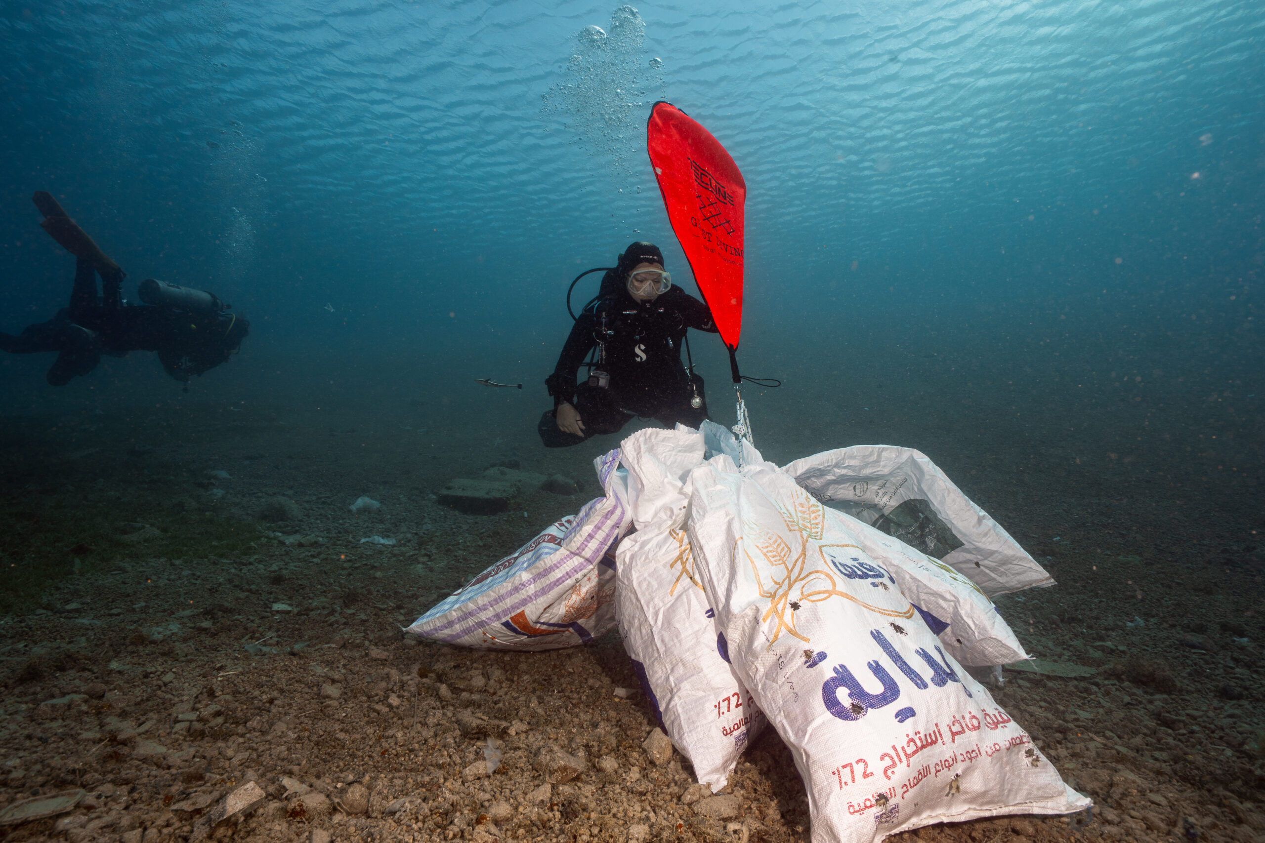 A diver raising a marker buoy over flour sacks filled with rubbish collected from the seabed in Dahab