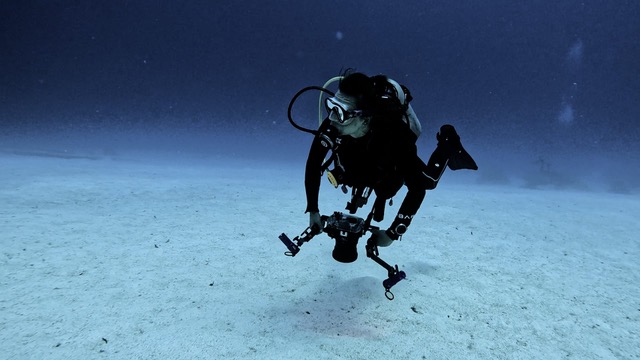 An underwater photographer hovering over the sand with a large camera rig