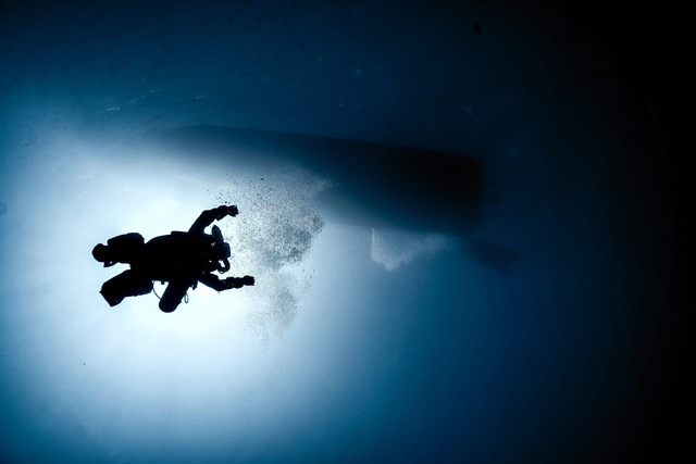 A diver silhouetted against the light beneath a liveaboard hull